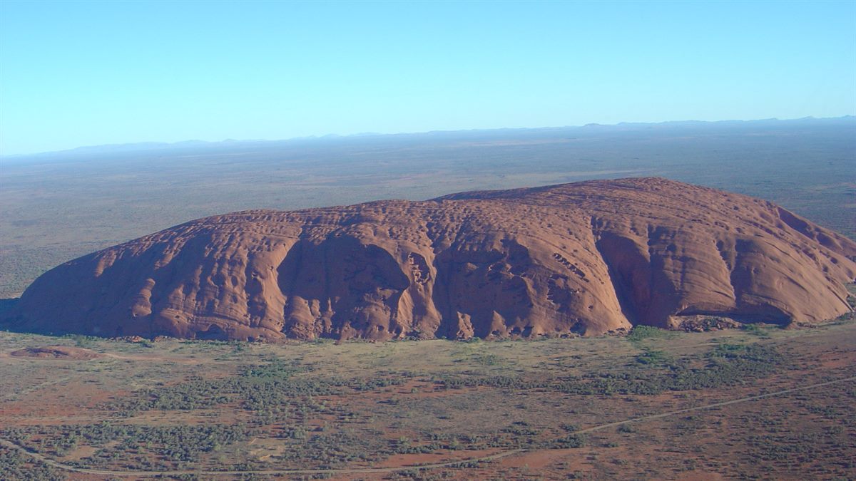 Uluru (Ayers Rock) no deserto australiano visto do alto, Austrália; paisagem natural e cultural ligada às tradições locais.